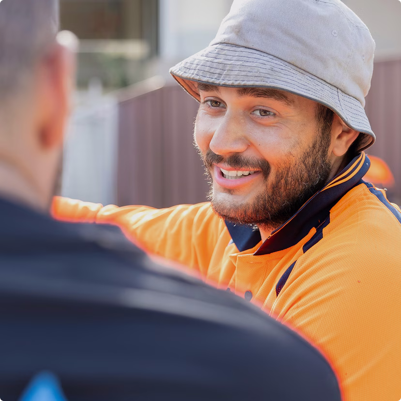 Australian construction worker, smiling outside and talking to another person.