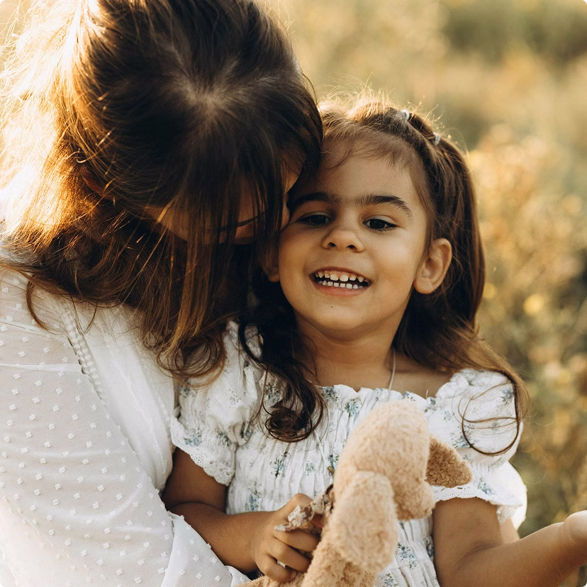 Mother and young daughter, together, outside in a field embracing.