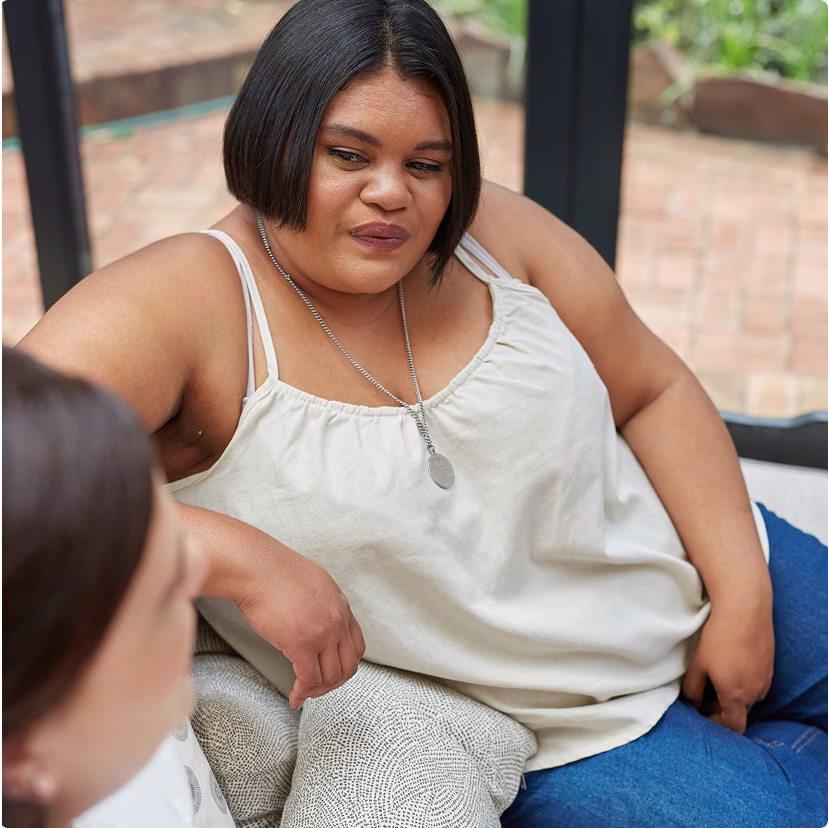 Women sitting on a couch, talking to another person.